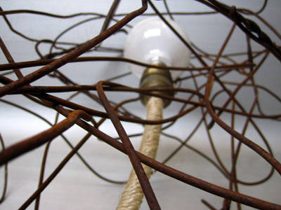 This lamp consists of a tangle of rusty wire, suspended from the top with the light fixture wire wrapped in hemp rope
